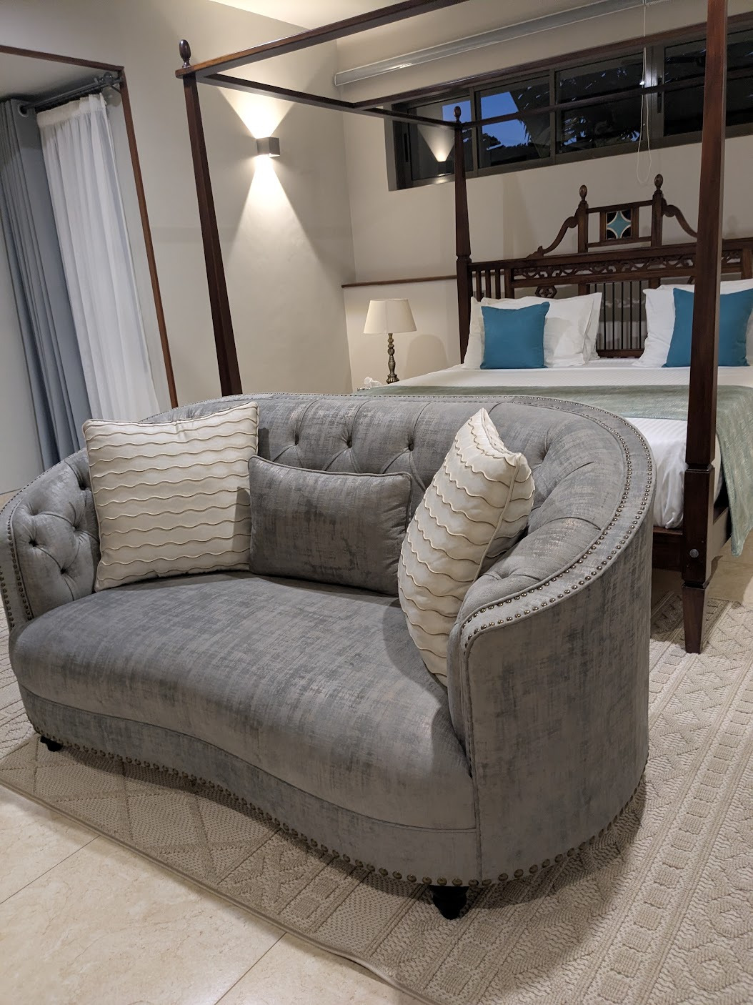 Master bedroom with a four-poster bed, teal accent cushions and a curved grey loveseat