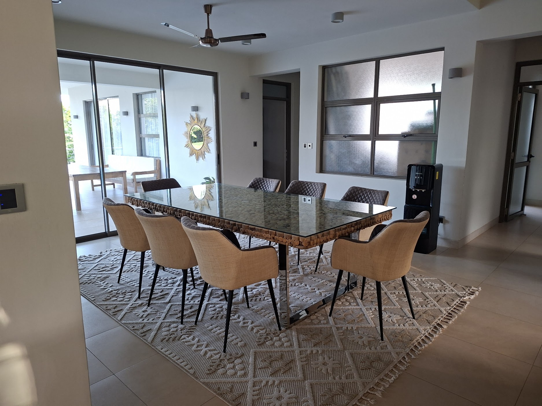 Dining room with a glass-topped statement table, woven chairs and a sunburst mirror