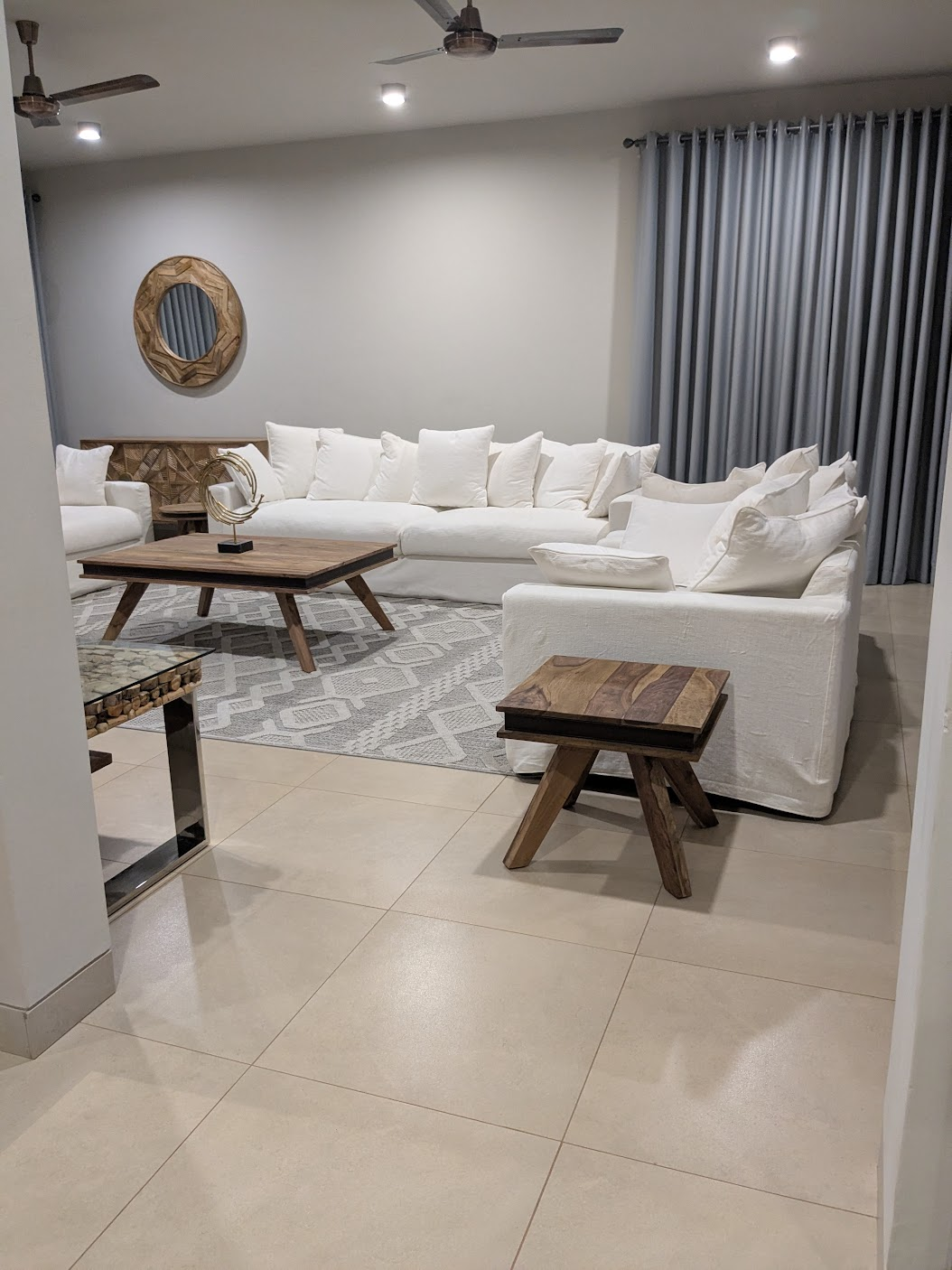 Second angle of the living room showing grey drape curtains and a wooden stool
